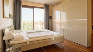 Un dormitorio moderno con una cama grande, una mesita de noche con lámpara, una puerta de cristal corredera y vistas al exterior.