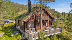 Une cabane avec des fondations en pierre, un revêtement extérieur en bois et un balcon doté de meubles pour se détendre à l’extérieur.