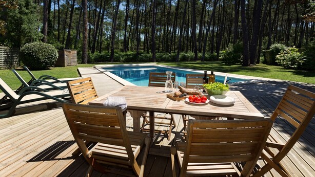 Una terrazza in legno con tavolo da biliardo, sedie e un tavolo apparecchiato con cibo e bevande.