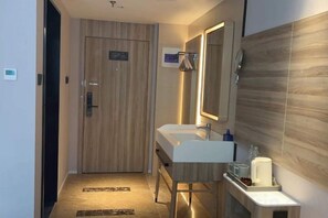 A modern bathroom with a wooden door, a sink, a mirror, and a towel rack. - HanTing Hotel (Xiamen Airport Wuyuan Bay) (Xiamen)