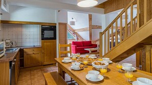 A kitchen with wooden cabinets, a dining table set with breakfast, and a staircase leading to an upper level. - La Cascade by Interhome (Vaujany)