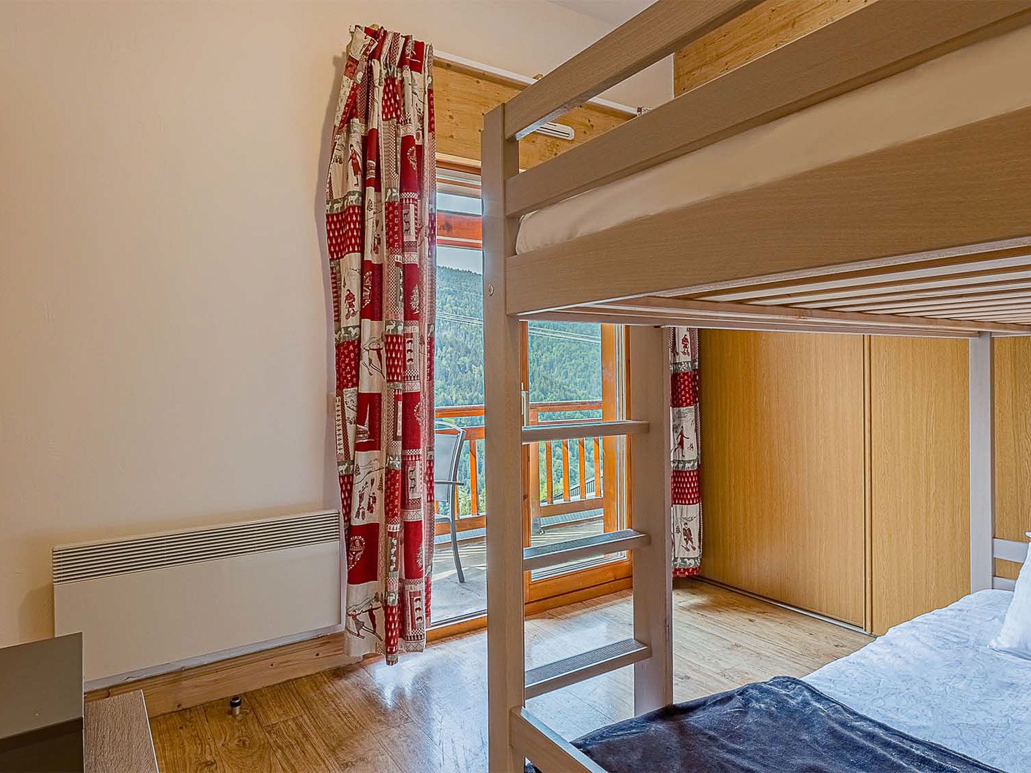 Ein Schlafraum mit Etagenbetten und Blick auf eine Holzterrasse sowie ein Fenster mit Vorhängen.