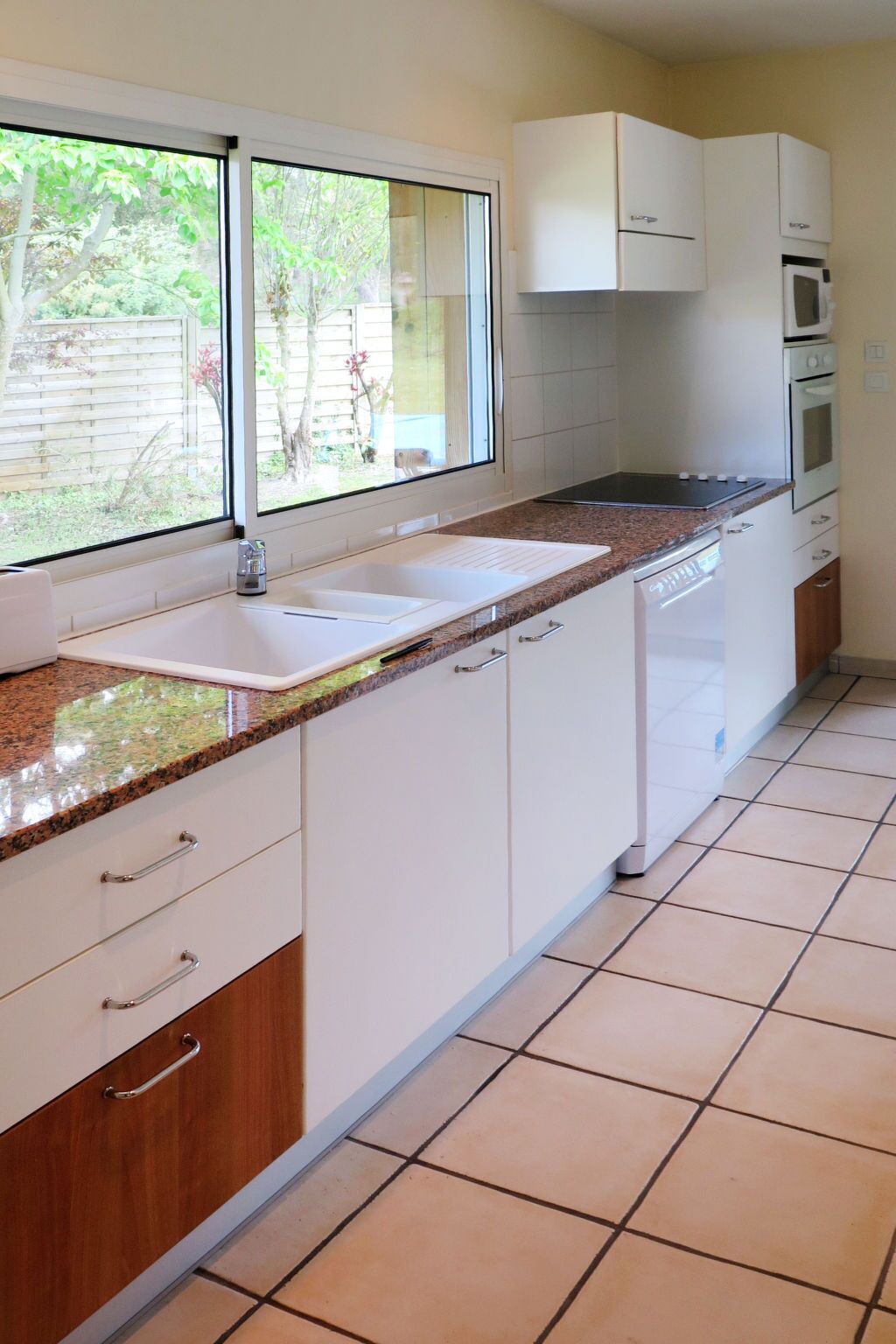 Een keuken met witte kastjes, een granieten aanrecht, een spoelbak en een raam met uitzicht op groen.