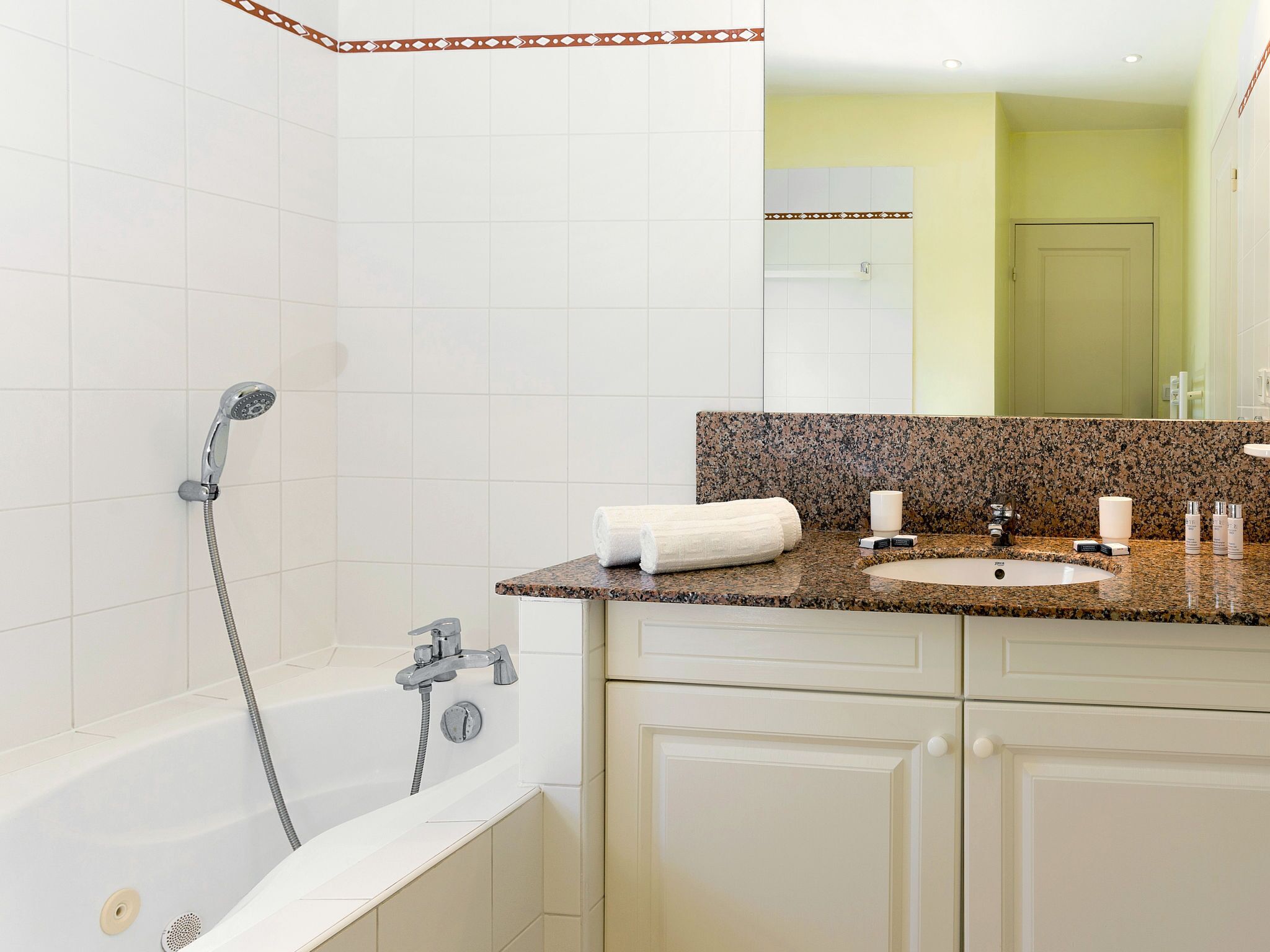Une salle de bain moderne avec une baignoire blanche, un lavabo surmonté d’un plan de travail en granit et un grand miroir.