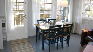 A dining area with a wooden table and chairs, large windows with curtains, a hanging light fixture, and a view of the outdoors. - Thorabu by Interhome (Eikerapen)