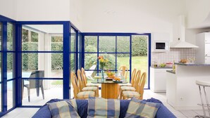 A modern kitchen with a dining area, large windows, and a view of a garden. - Club Royal Aquitaine by Interhome (Moliets)