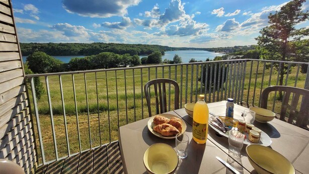 Ein Balkon mit Frühstückstisch, mit Blick auf einen See und einen Wald.