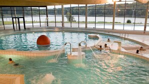 Ein Hallenbad mit verschiedenen Wasserspielen und Blick auf einen See durch große Fenster.