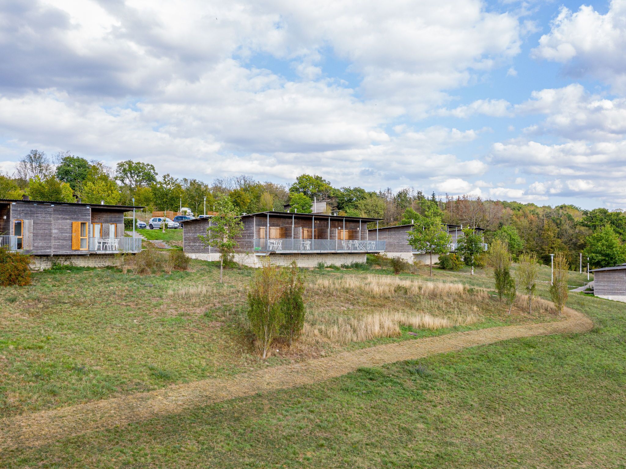 Eine moderne, zweistöckige Holzhütte mit Balkon, umgeben von einer Wiese und Bäumen.