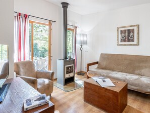 A living room with a sofa, armchair, and a coffee table. A fireplace is visible in the corner, and there is a window with curtains.