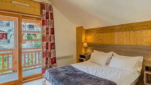 A bedroom with a wooden headboard, a bed with white linens, a red and white curtain, and a view of a building through a glass door. - La Cascade by Interhome (Vaujany)