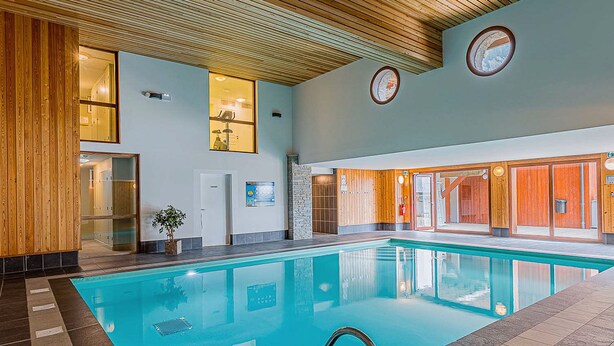An indoor swimming pool with a wooden ceiling, glass walls, and a tiled floor. - La Cascade by Interhome (Vaujany)