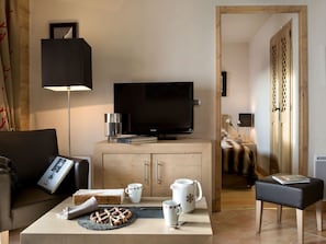 A modern living room with a flat-screen TV, a coffee table with a plate of food, and a sofa.