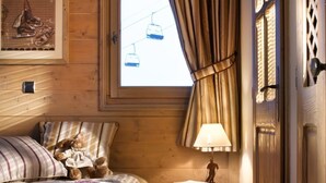 Un dormitorio acogedor con piso de madera, una cama con ropa de cama floral, una mesita de noche con lámpara y una ventana con cortinas.