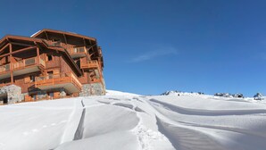 Una cabaña de madera con base de piedra, varios balcones y una pista de esquí al fondo.