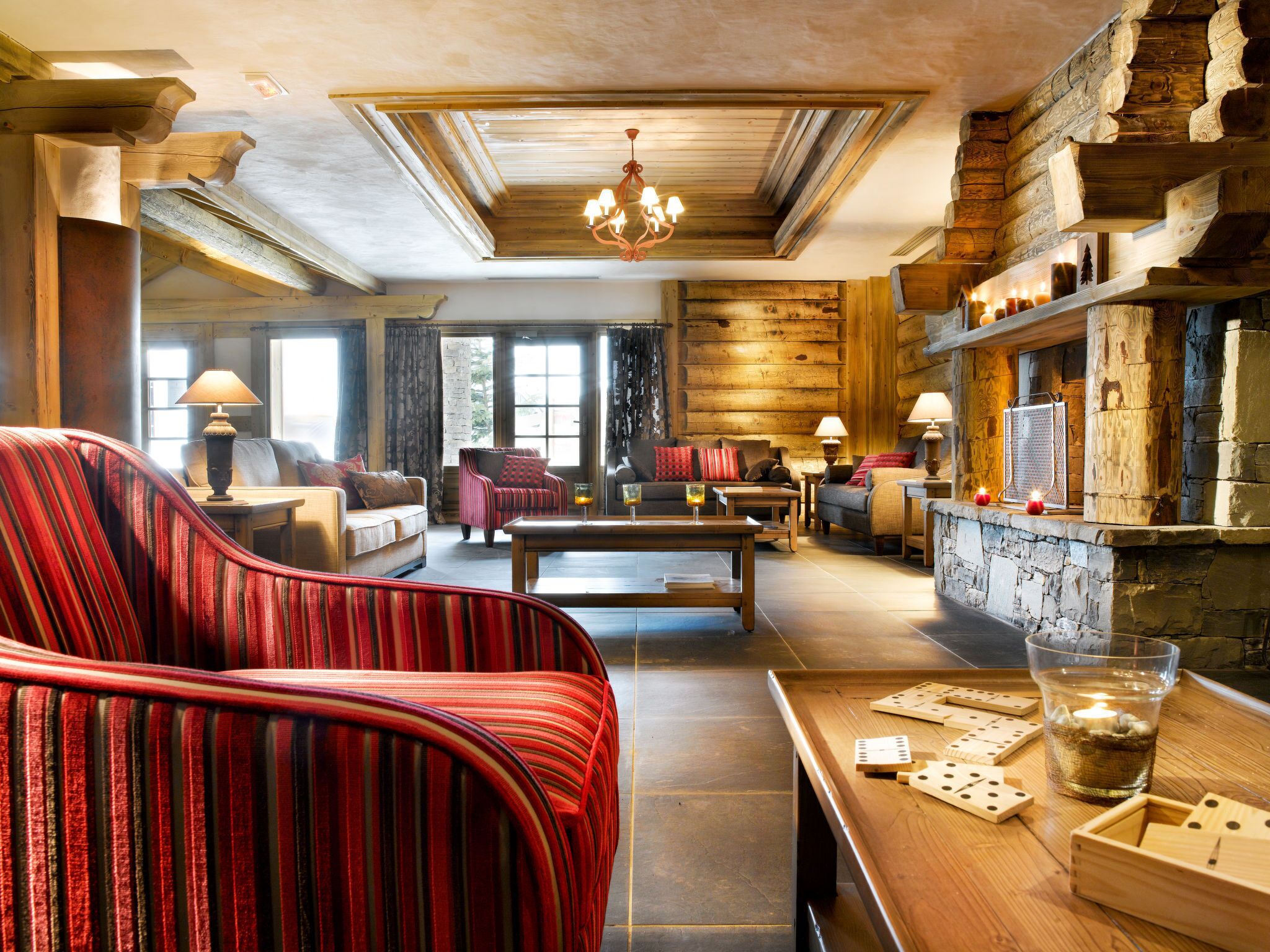 A cozy living room with a fireplace, wooden beams, and a chandelier. There are multiple seating areas with sofas and a coffee table.