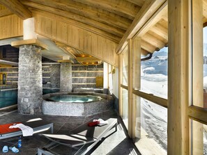Et spaområde med en stensøjle, jacuzzi og udsigt til et sneklædt landskab gennem store vinduer.