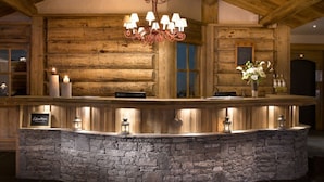 Interior de una cabaña de troncos con chimenea de piedra, vigas de madera y un candelabro.