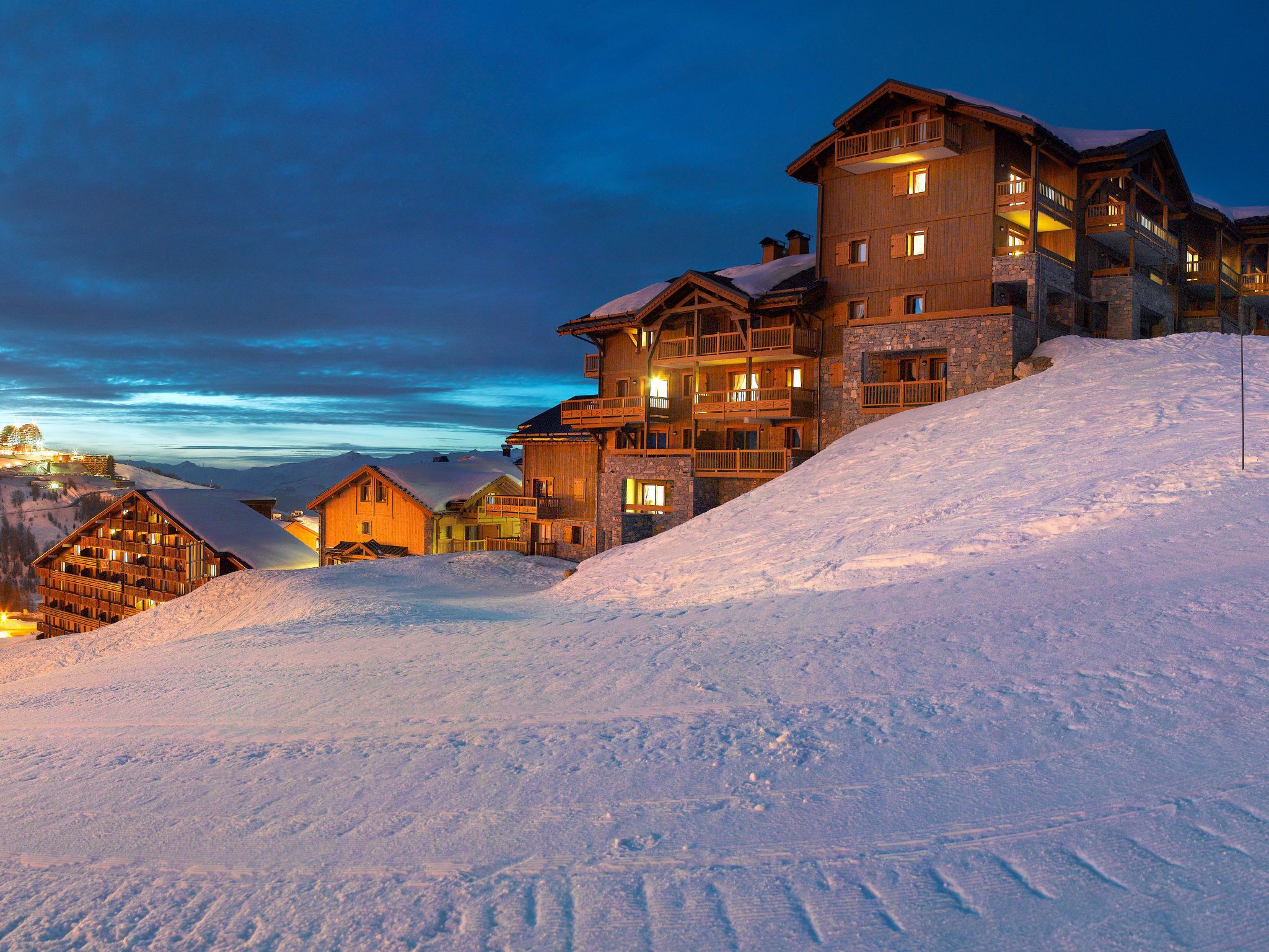 A multi-story lodge with balconies, situated on a snow-covered slope.