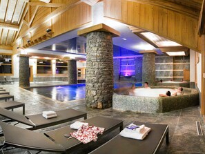 A spa area with stone pillars, a pool, and lounge chairs.