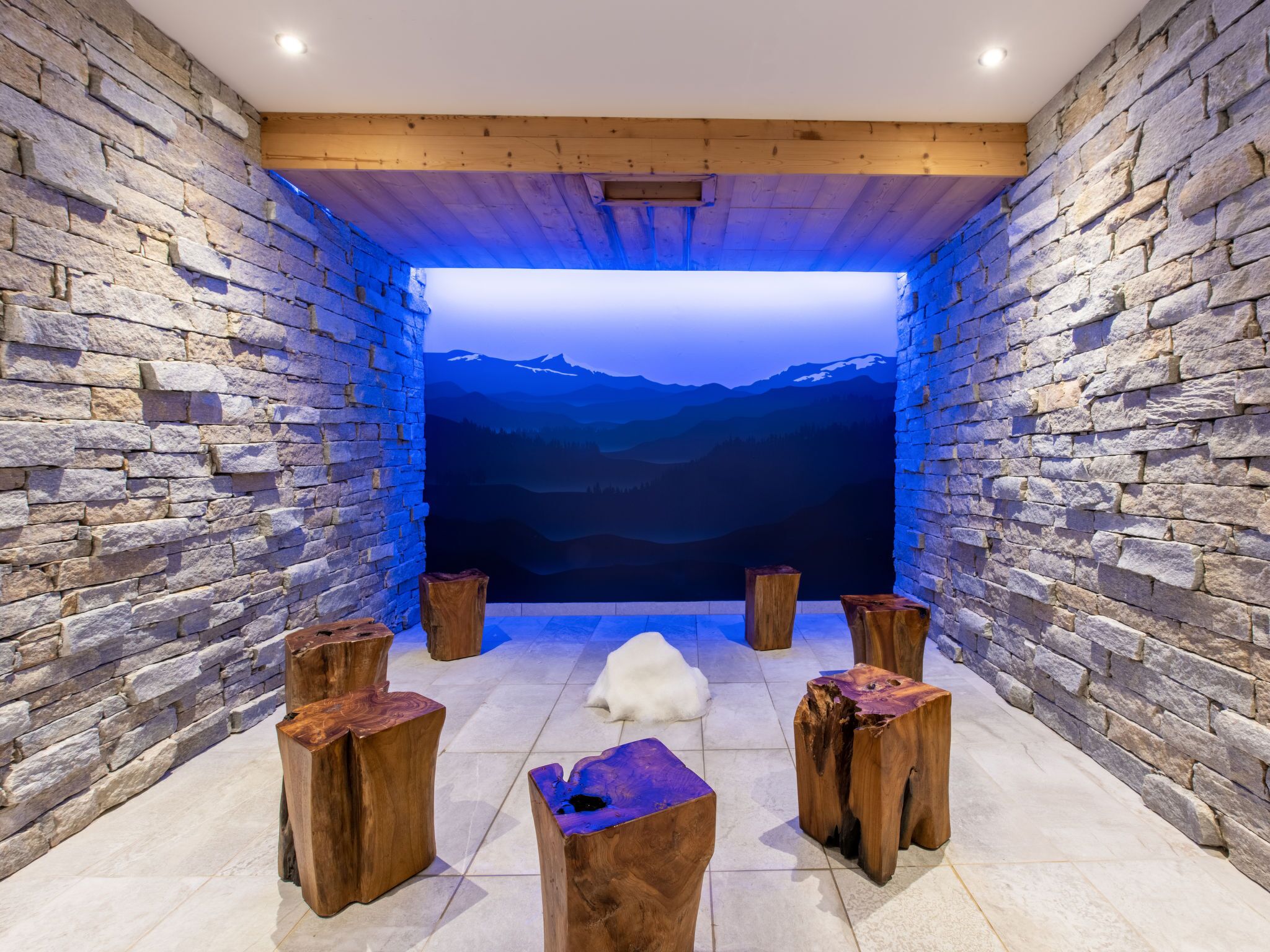 Quarto com paredes de pedra, teto de madeira, uma janela grande e quatro banquetas de madeira.