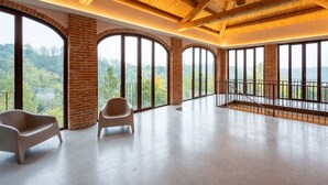 Een ruime kamer met grote, gebogen ramen en uitzicht op een bebost landschap.