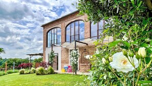 Een modern huis van baksteen met grote ramen, een verzorgd gazon en diverse bloeiende planten.