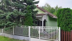 A green house with a white fence, a red roof, and a small porch.