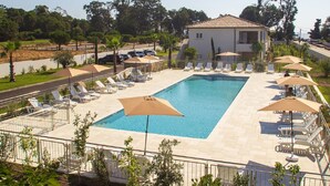 A swimming pool with sun loungers and umbrellas, surrounded by a fence and trees.