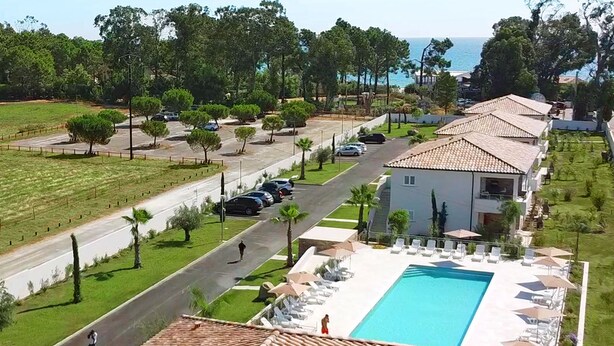 A resort with a swimming pool, beachfront view, and a road with parked cars.