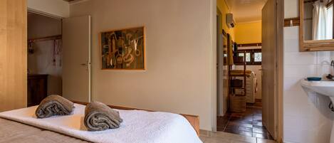 A bedroom with a bed, a painting, and a bathroom visible through an open door.