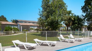 A swimming pool with white lounge chairs and a fenced area with greenery and buildings in the background. - A Suara by Interhome (Ghisonaccia)