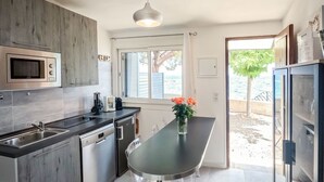 A modern kitchen with grey cabinets, a stainless steel microwave, a built-in oven, and a dining area with a table and chairs. - Dentice by Interhome (Solenzara)