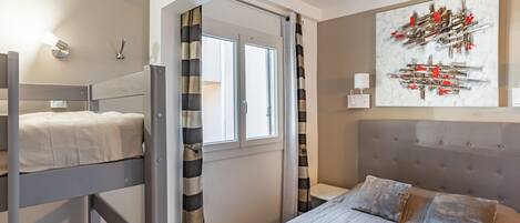 Un dormitorio con literas, una cama individual, una ventana con cortinas, una lámpara de pared y una obra de arte abstracta.