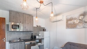 A modern kitchen with a built-in microwave, oven, and coffee maker. There is a dining table with chairs and a gray sofa in the living area.