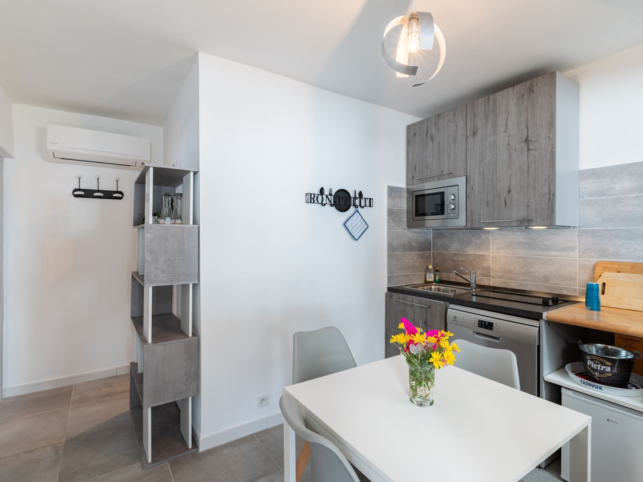A modern kitchen with white cabinetry, a microwave, and a sink. There is a dining table with a vase of flowers.