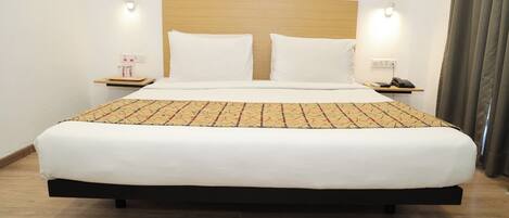 A hotel room with a large bed, two bedside tables, a wooden headboard, and a patterned bedspread.