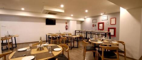 A dining area with multiple tables and chairs, a fire extinguisher on the wall, and framed pictures on the wall.