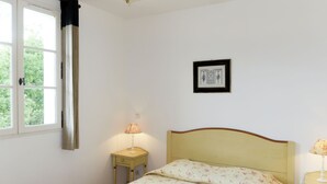 A bedroom with a bed, a bedside lamp, a window with curtains, and a framed picture on the wall. - Domaine de Fayence M24 by Interhome (Fayence)