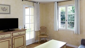 A room with a television on a cabinet, a wooden chair, a table, and two windows with curtains. - Domaine de Fayence M24 by Interhome (Fayence)