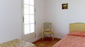 A room with two single beds, a chair, a window, and a small picture on the wall.