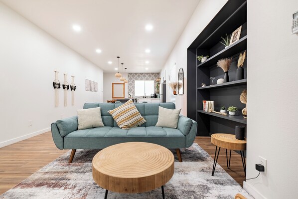 Een moderne woonkamer met een turquoise bank, een houten bijzettafeltje en een vloerkleed met dessin.