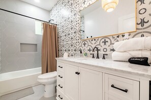 Een moderne badkamer met een wit toilet, een badkuip, een wastafel met spiegel en betegelde vloeren.