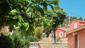 A gravel driveway leading to a red building with a white door, surrounded by greenery and a stone wall. - Le Cabanon by Interhome (Draguignan)