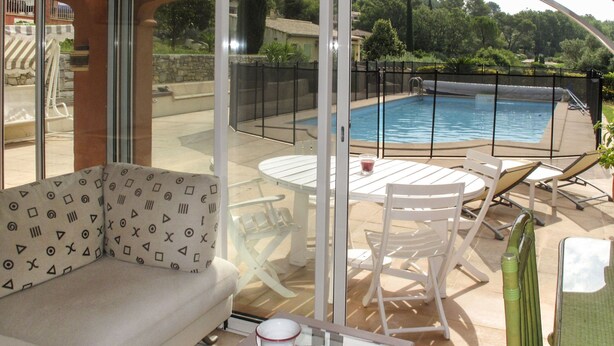 An outdoor patio with a pool, white furniture, and a glass-enclosed area. - Le Cabanon by Interhome (Draguignan)