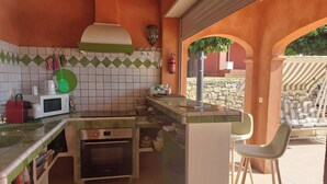 A compact kitchen with a microwave, toaster, and oven. There is a small bar area with stools and a stone wall in the background. - Le Cabanon by Interhome (Draguignan)