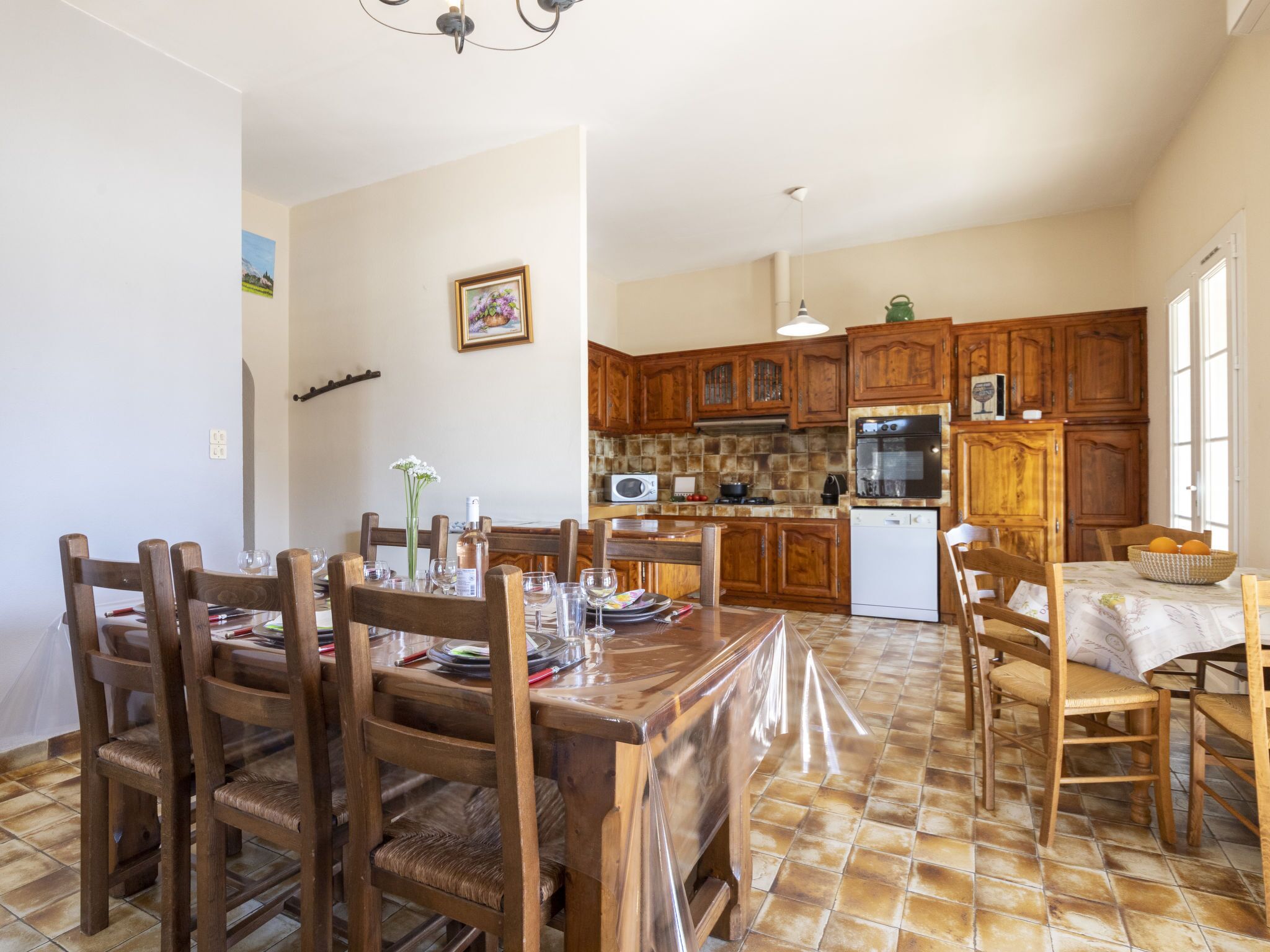 Zona pranzo con tavolo e sedie in legno, cucina con mobili in legno, microonde e frigorifero.