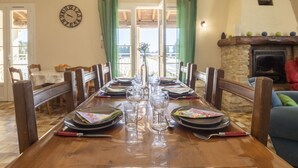 A dining room with a wooden table set for four, a clock on the wall, and a fireplace in the background. - Mas de la Gourmette by Interhome (Châteaurenard)