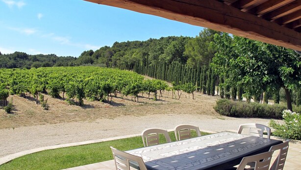 A patio with a table and chairs, overlooking a vineyard.