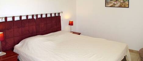 A neatly made bed with a red headboard, a bedside table with a lamp, and a framed picture on the wall.